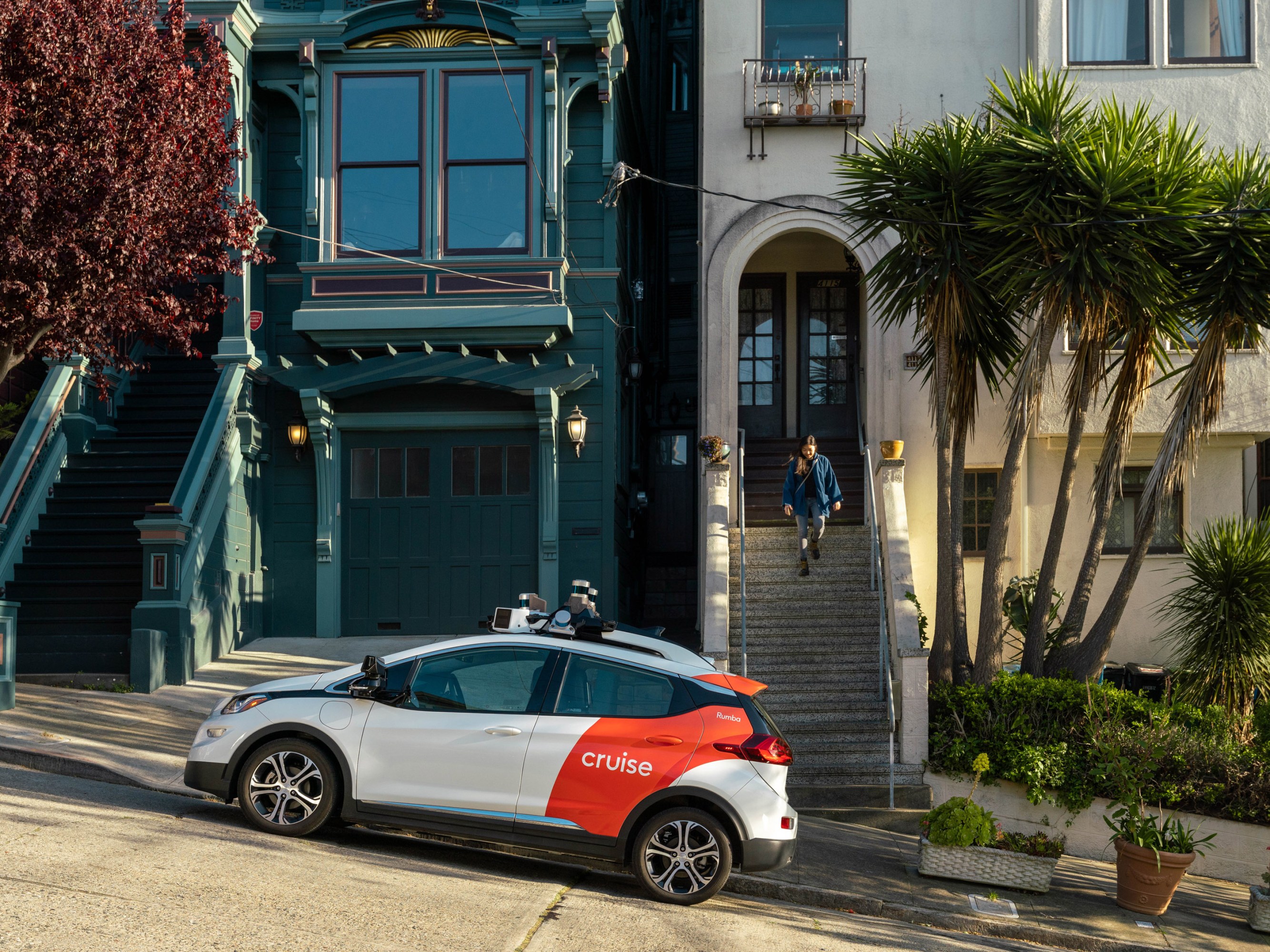 a Cruise vehicle parked on the street in front of a residential home as a person descends a front staircase in the background